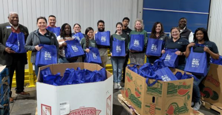 A group of about a dozen volunteers stand with bags in front of bins at an event to help empower women.