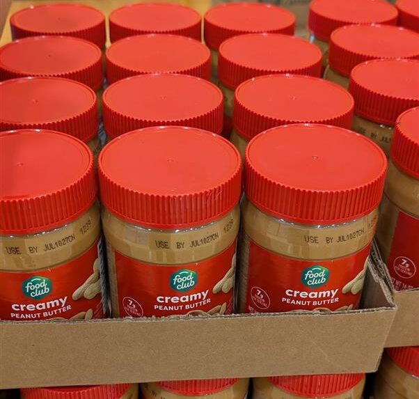 Food Club Creamy Peanut Butter jars stacked in cardboard trays at a community event.
